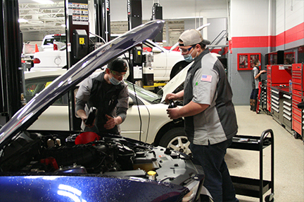 two students changing oil on a blue car